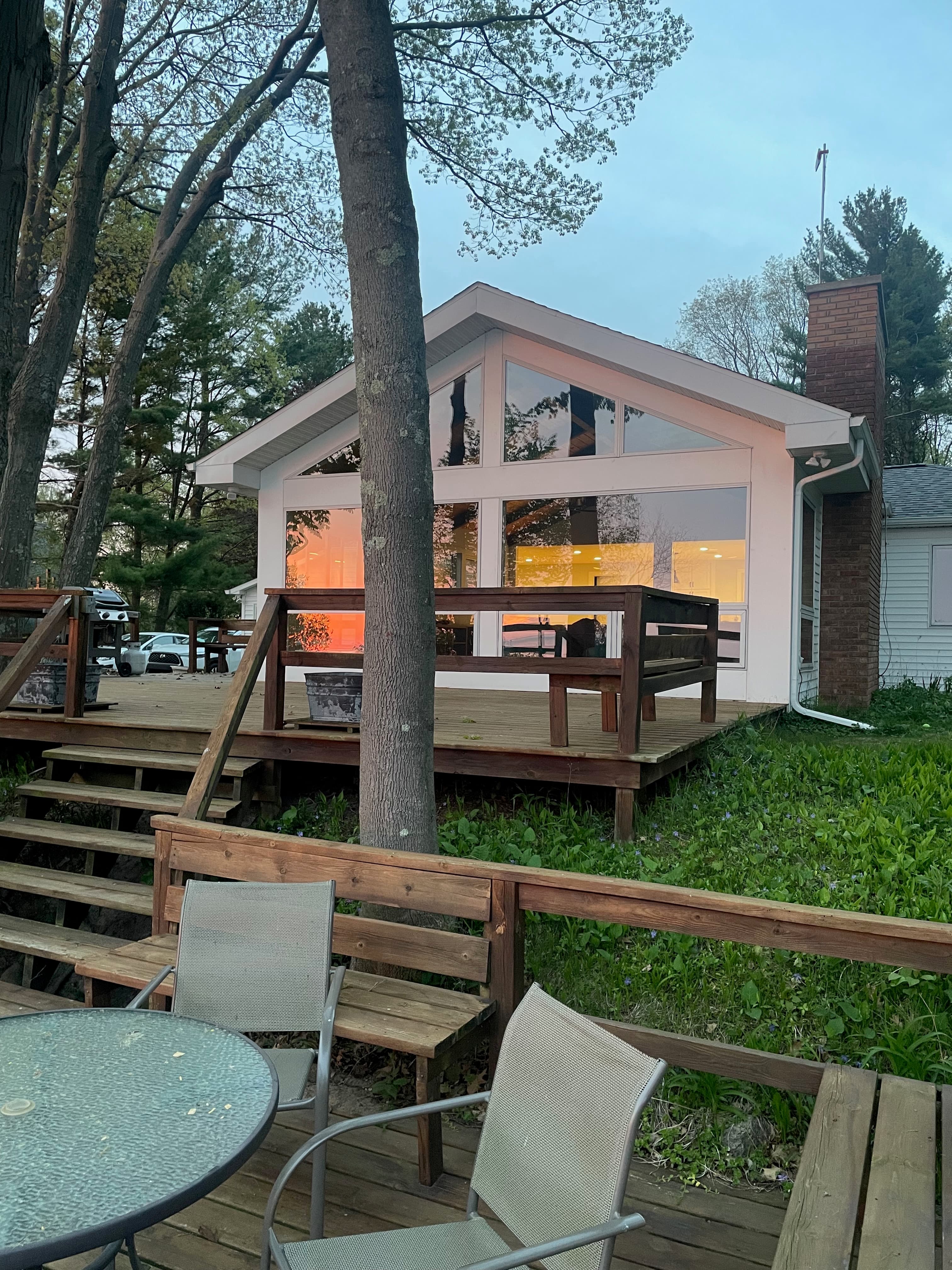 Cottage exterior at dusk showing A-frame windows, multi-level deck, and mature oak trees