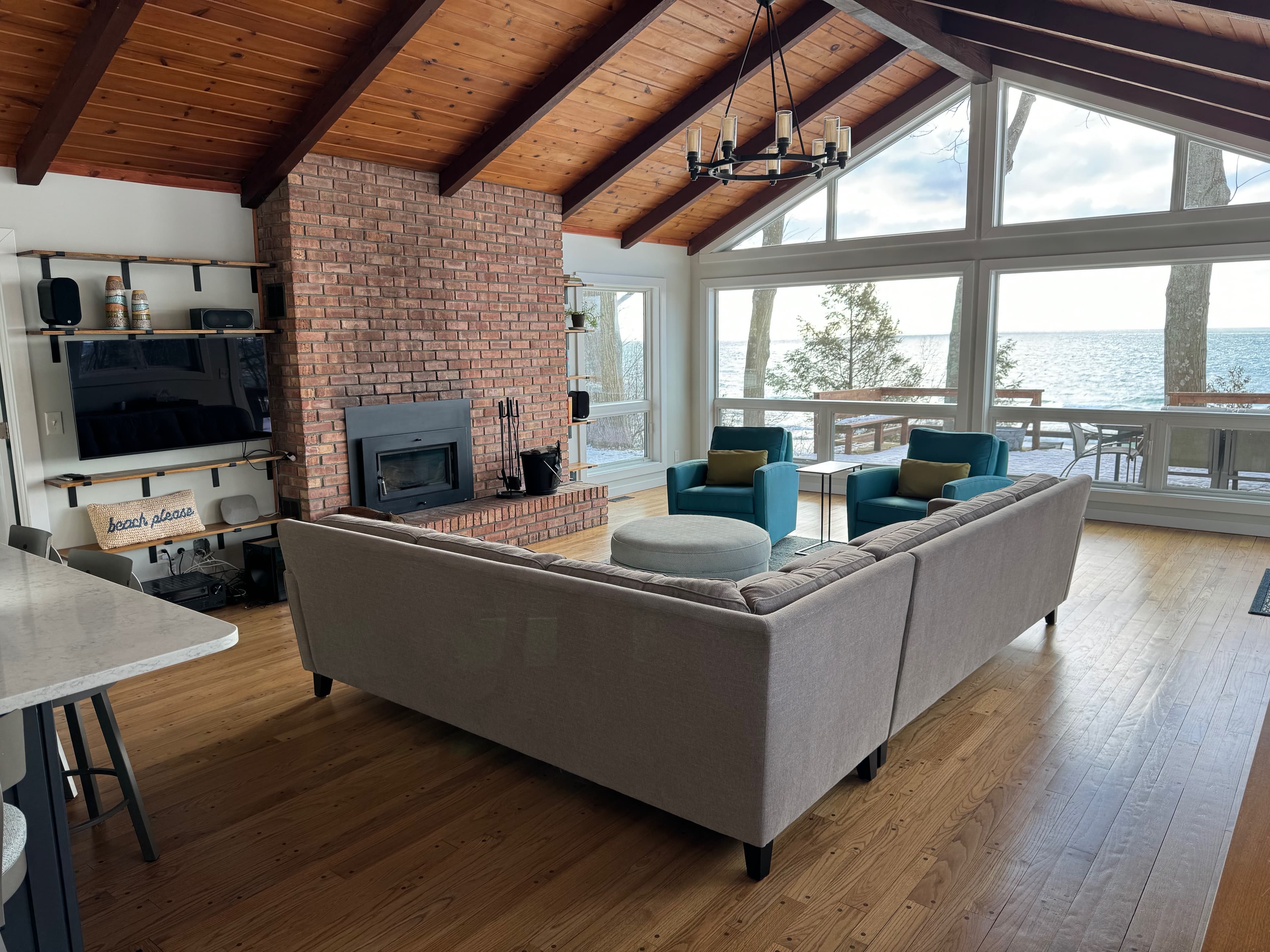 Living room with wood-burning stove, vaulted cedar ceiling, and wall of windows facing Lake Michigan