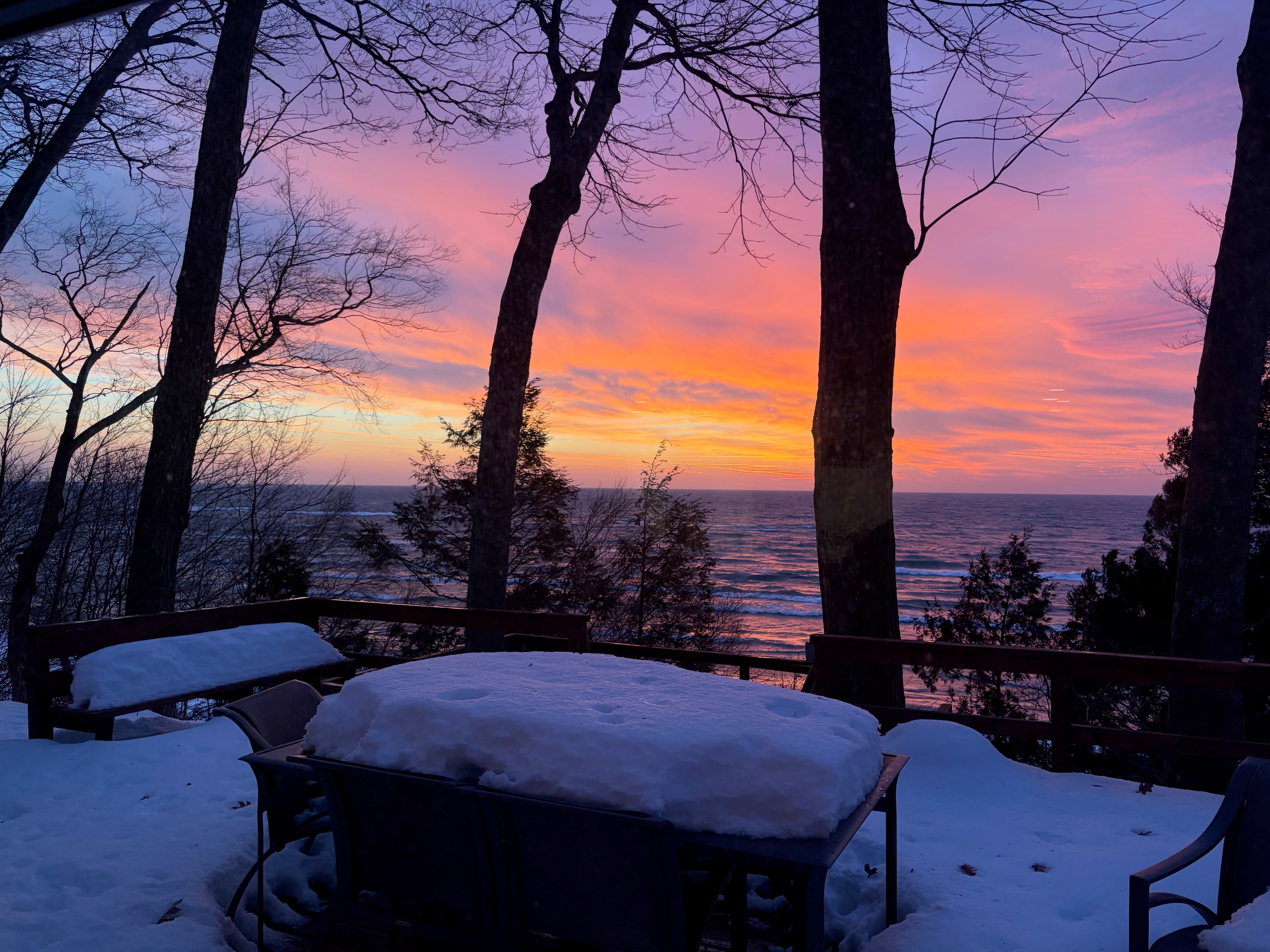 Winter sunset from snow-covered deck with vibrant purple and orange sky over frozen Lake Michigan