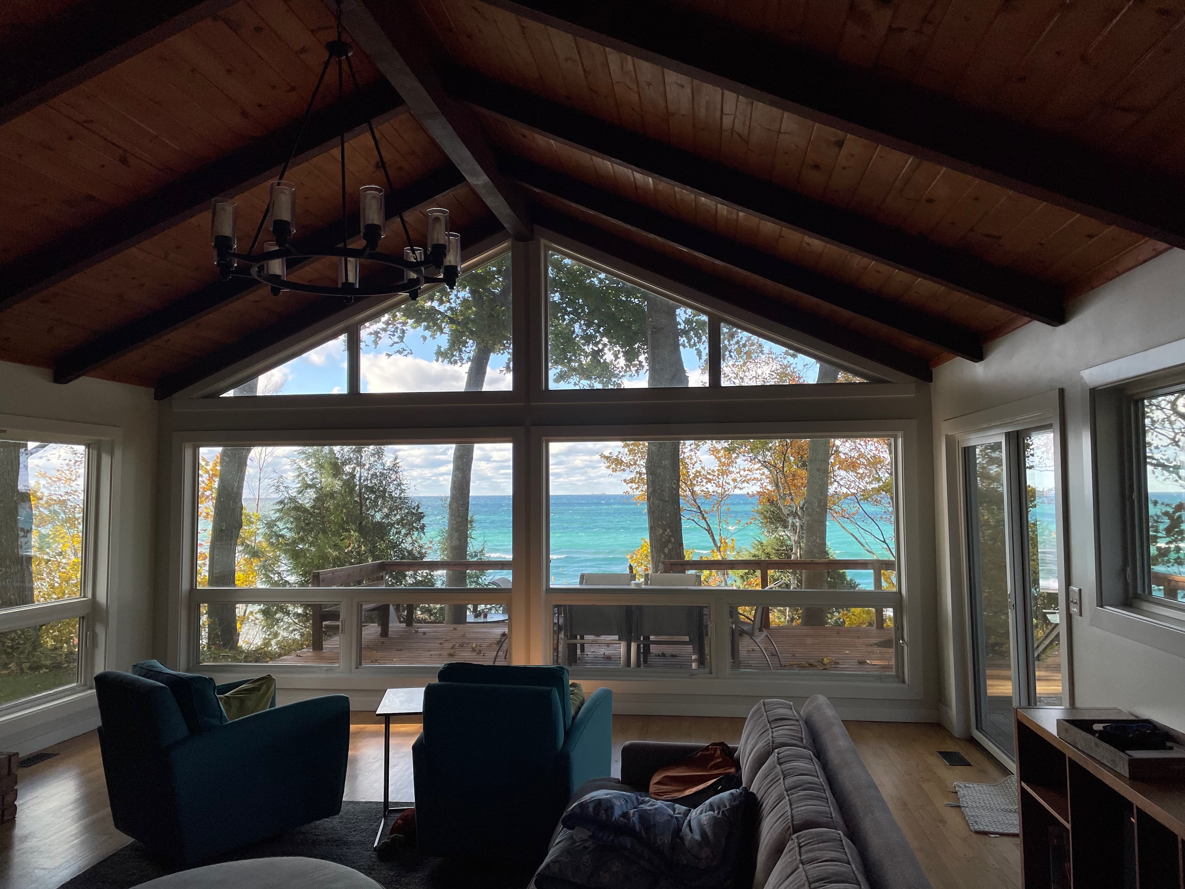 Living room in autumn with turquoise accent chairs, vaulted ceiling, and panoramic lake views through oak trees